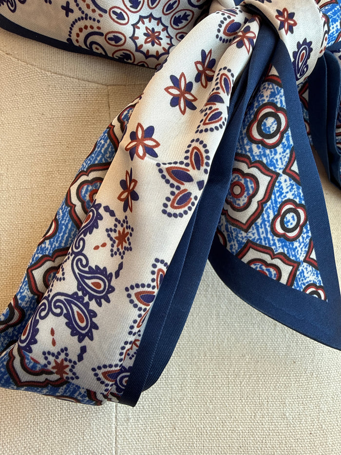 Blue paisley twilly scarf detail with cream base, navy circles, red flowers, and flowing ribbons