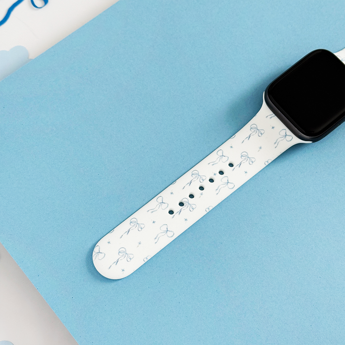 Coconut Lane Bluebell Bows Apple Watch strap with blue bow pattern on a light blue surface.