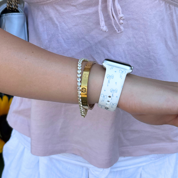 Bluebell Bows patterned Apple Watch strap with gold and diamond bracelets, worn with a pink top.