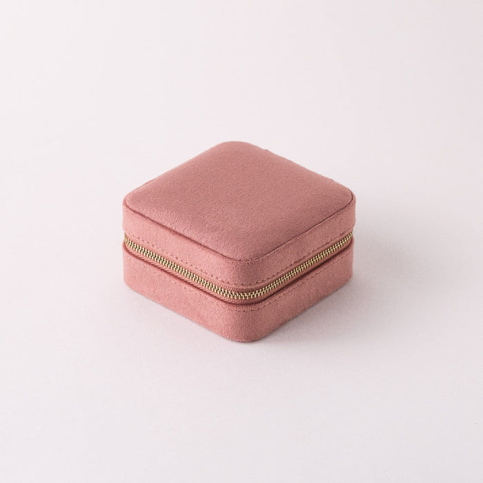 A compact square travel case in rose quartz color with a gold coloured zipper.