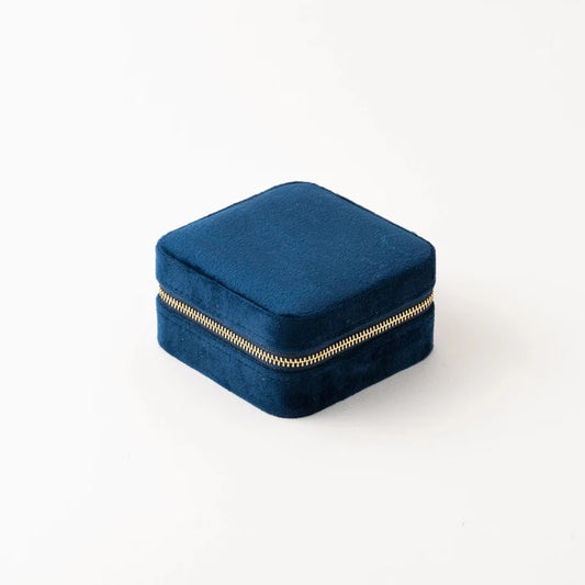 A compact square travel case in blue velvet with a gold coloured zipper.