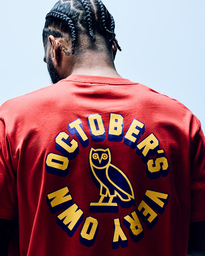 Red t-shirt with yellow and navy circular wordmark graphic featuring an owl design on back.