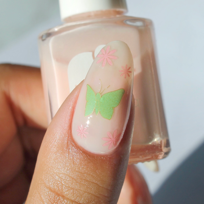 Come Fly With Me butterfly nail decal on a sheer nude nail, holding the bottle