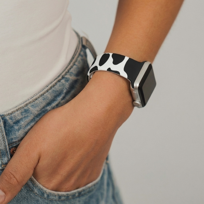 Hand with Coconut Lane cow print Apple Watch strap rests in the pocket of blue jeans.