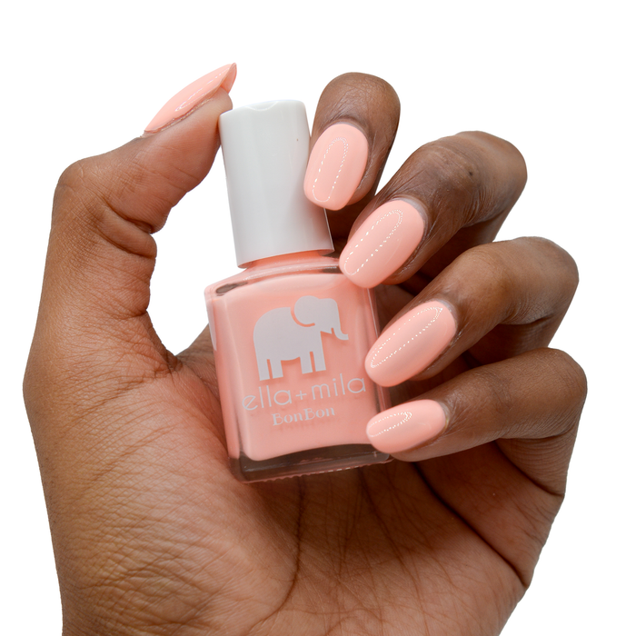 Creamsicle creamy peach pink nail polish on a deep skin tone, hand holding the bottle