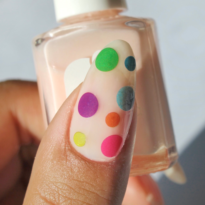 Dot Dot Dot colorful polka dot decals on a sheer nude nail, holding the bottle