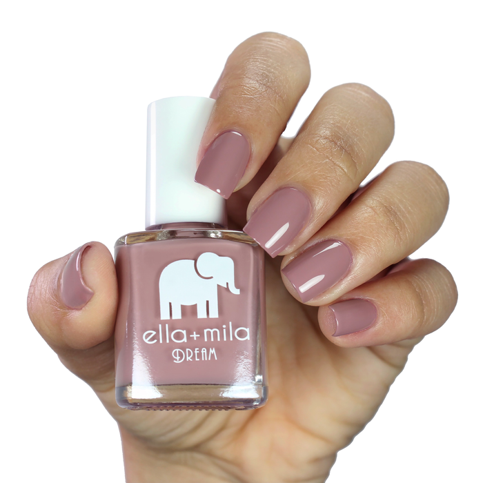 Dreamcatcher dusty nude purple nail polish on a medium skin tone, hand holding the bottle