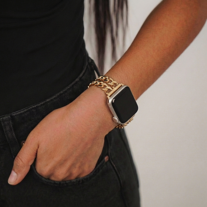 Gold Coconut Lane Dual-Chain Apple Watch strap on wrist, hand tucked into pocket of black jeans.