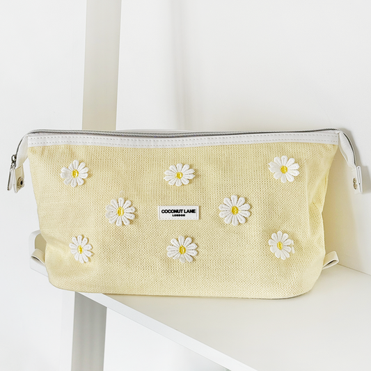 Buttercup yellow expandable makeup bag with white daisy pattern on a white shelf.