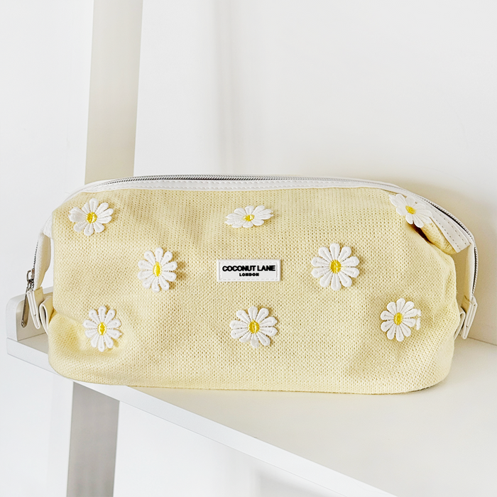 Buttercup Bloom expandable makeup bag by Coconut Lane in soft yellow with floral pattern on a white shelf.