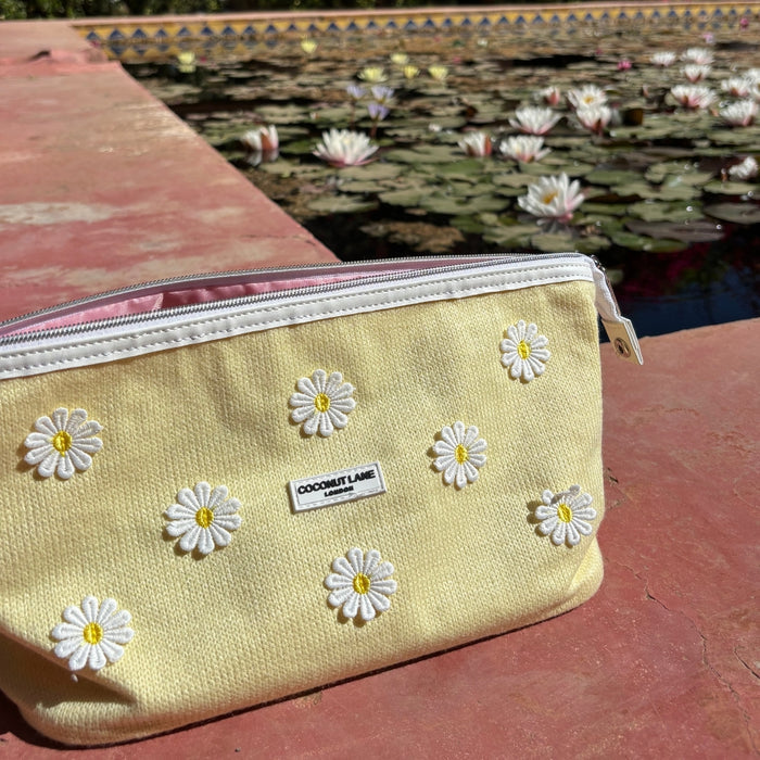 Coconut Lane Buttercup Bloom expandable makeup bag with floral print on a red surface near lily pads and white flowers.