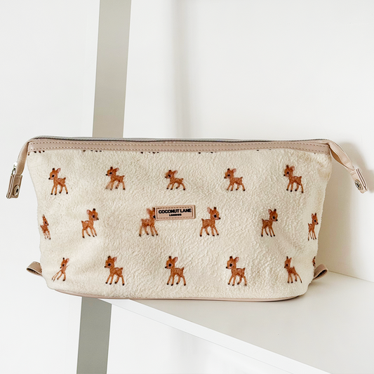Cream-colored expandable makeup bag with deer print by Coconut Lane, resting on a white shelf.