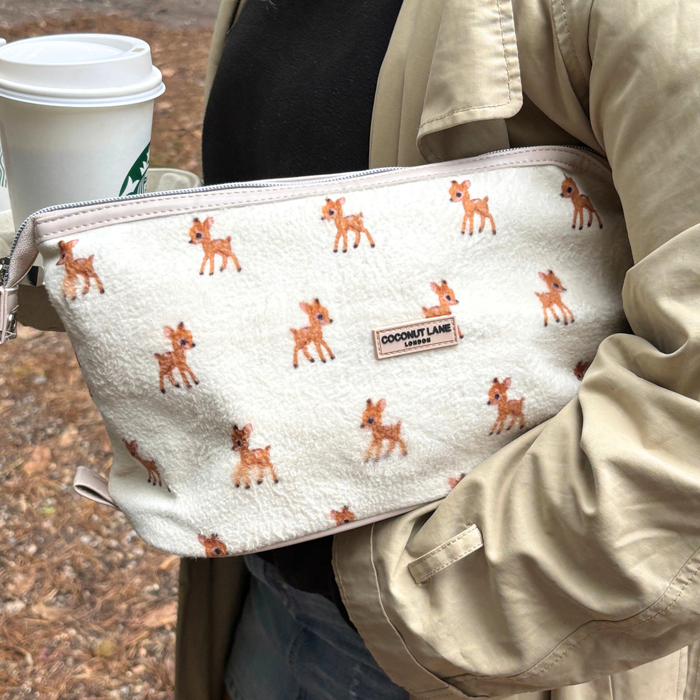 Person holding a coffee cup and Coconut Lane expandable makeup bag in white fleece with deer print.