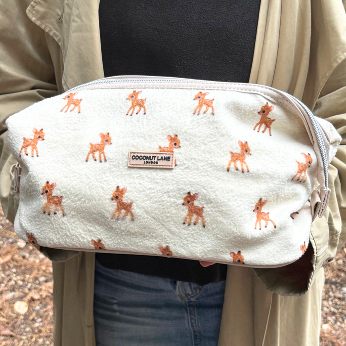 Expandable makeup bag in light fabric with small deer print, held in hand.