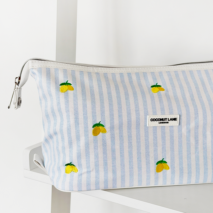 Expandable makeup bag with light blue and white stripes, lemon pattern, by Coconut Lane, on a white shelf.