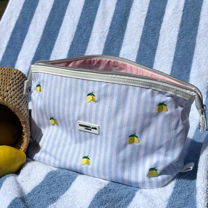 Yellow lemon-patterned expandable makeup bag from Coconut Lane on a towel next to a woven basket.