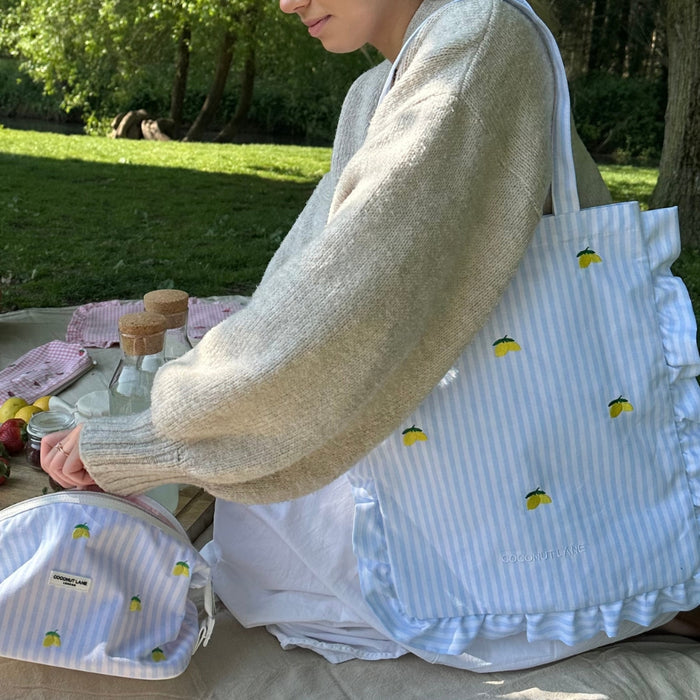 Yellow lemon-print expandable makeup bag from Coconut Lane on a picnic blanket outdoors in a park.