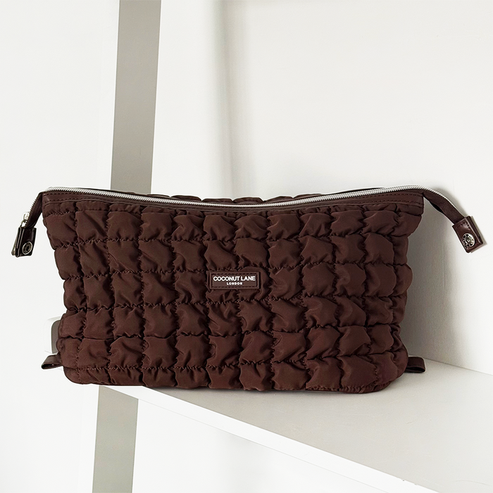 Quilted chocolate brown expandable makeup bag by Coconut Lane on a white shelf.