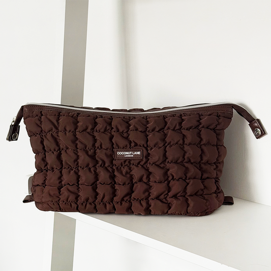 Quilted chocolate brown expandable makeup bag by Coconut Lane on a white shelf.
