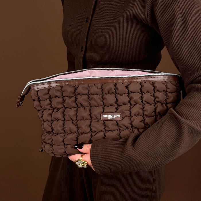 Expandable brown quilted makeup bag from Coconut Lane held by person, set against a matching brown background.