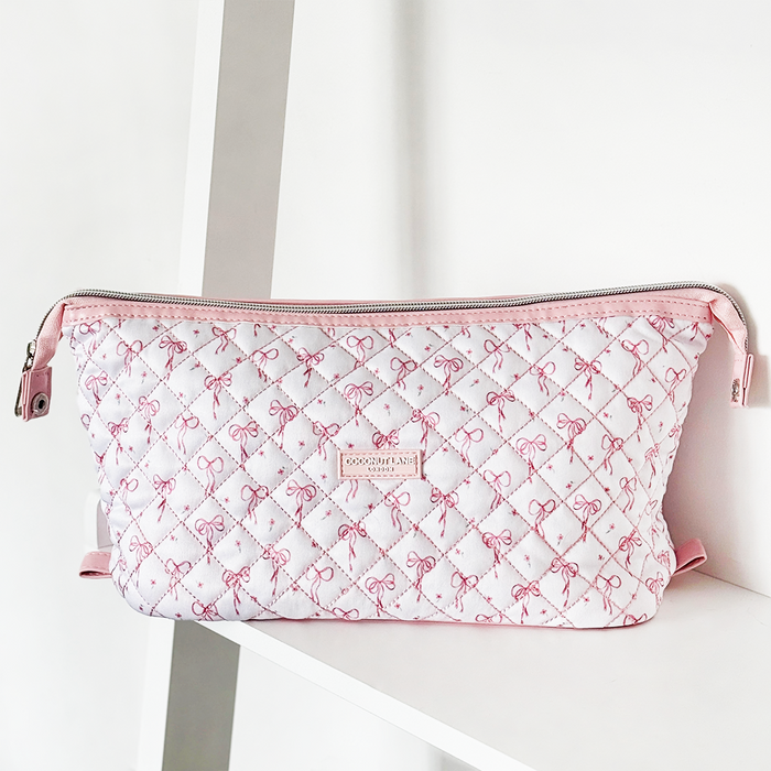 Pink and white quilted makeup bag with dainty bow pattern, displayed on a white shelf.