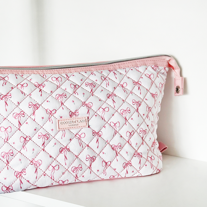 Quilted Coconut Lane expandable makeup bag with white and pink bow pattern, shown on a white surface.