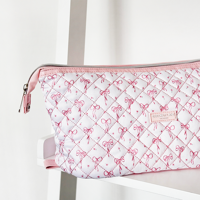Pink and white quilted Coconut Lane expandable makeup bag with dainty bow pattern on a white shelf.
