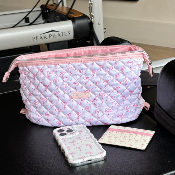 Pink and white quilted makeup bag with dainty bows on a Pilates machine, next to a phone and cardholder.