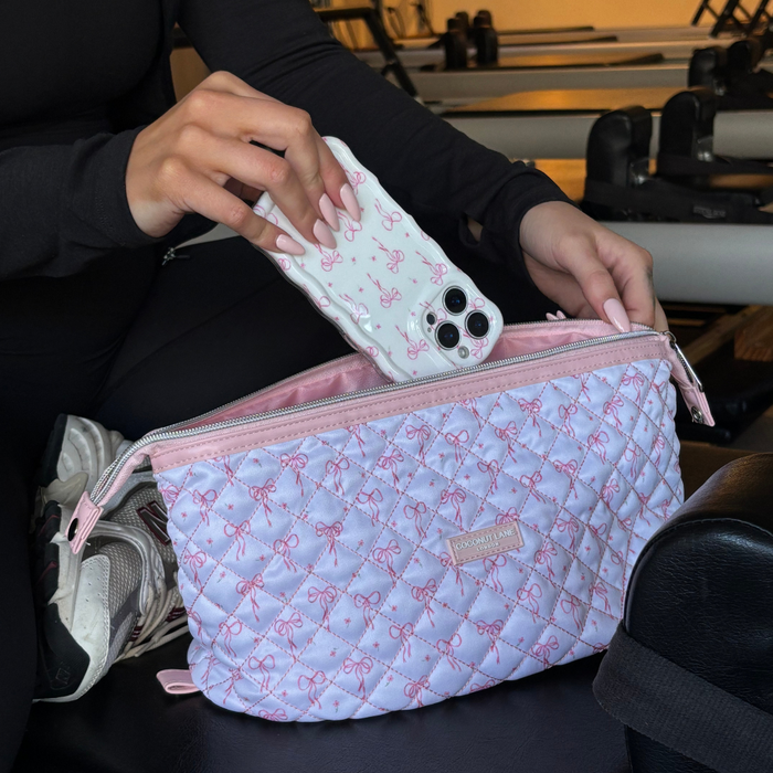 Pink quilted gym bag with bow print and matching expandable makeup bag on the floor of a pilates studio.
