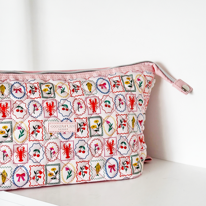 Quilted makeup bag with colorful stamp pattern, displayed on a white shelf.