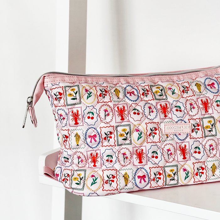 Pink quilted Dolce Vita expandable makeup bag by Coconut Lane with colorful patterns, displayed on a white shelf.