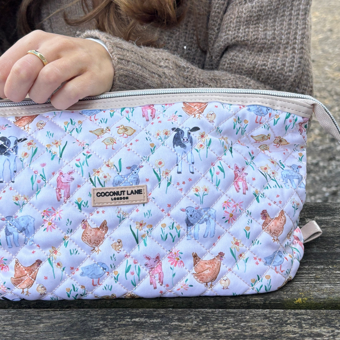 Person in brown sweater holding a quilted Coconut Lane makeup bag with a colorful farm animal print.