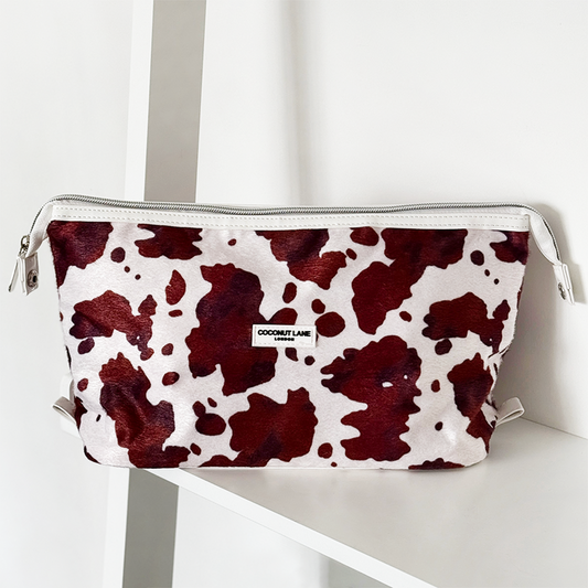 Expandable makeup bag with red and white cow print on a white shelf.