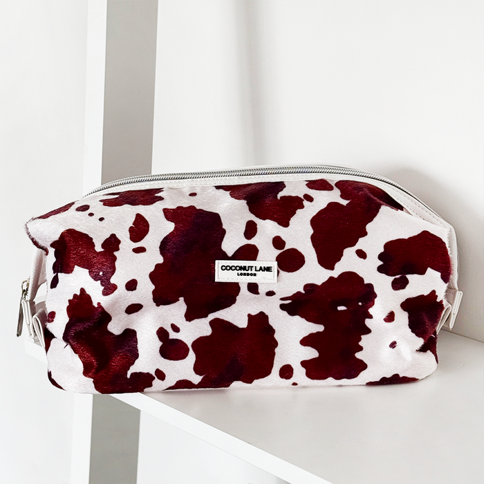Cow-print Expandable Makeup Bag with zipper by Coconut Lane on a white shelf.