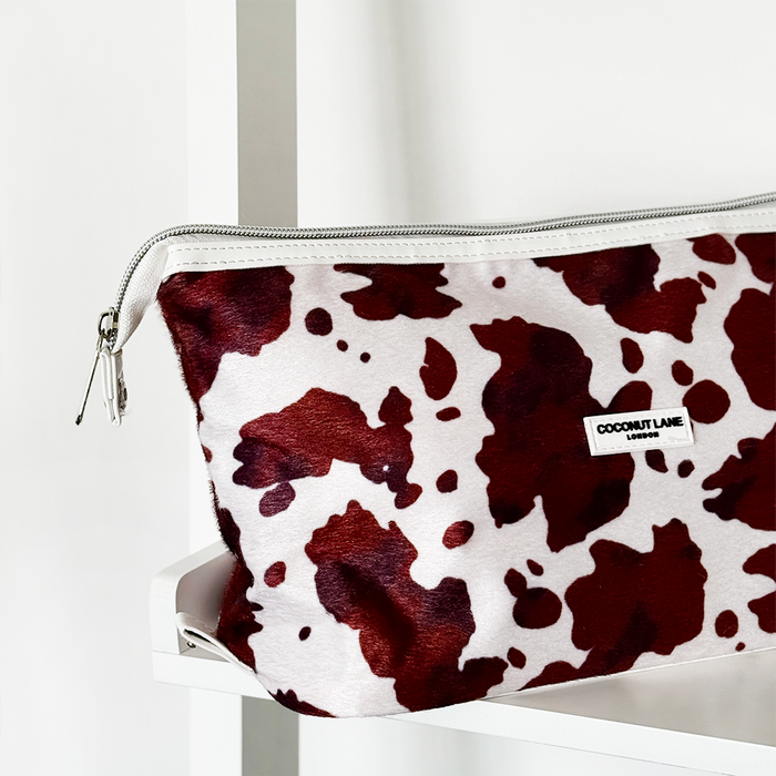 Brown and white cow print expandable makeup bag on a white shelf.