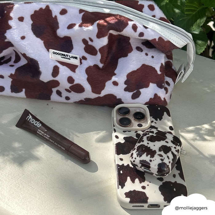 Cowgirl-patterned makeup bag, iPhone and AirPods cases, brown makeup stick on green leafy background.