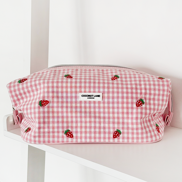 Expandable makeup bag with a strawberry print by Coconut Lane on a white shelf.