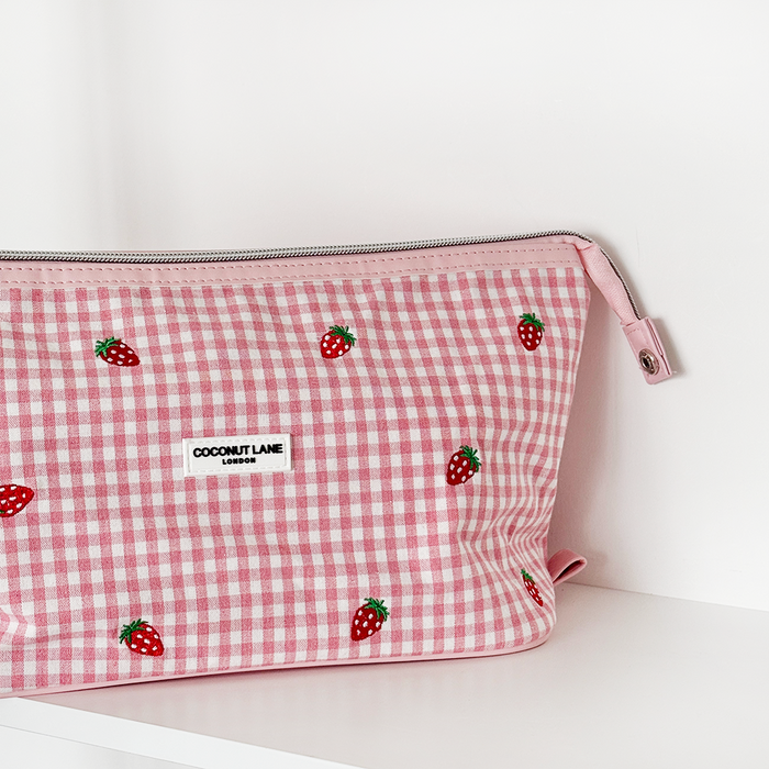 Coconut Lane expandable makeup bag with a pink and white checkered pattern and strawberry prints on a white surface.
