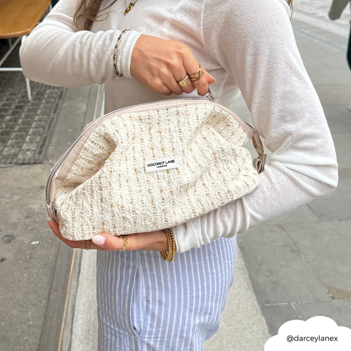 Woman in a white top holds a vanilla tweed Coconut Lane expandable makeup bag on a city sidewalk.