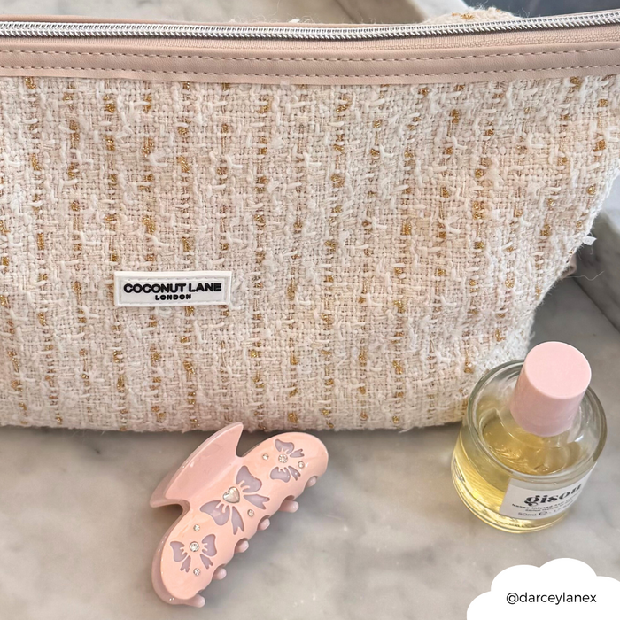 Vanilla tweed Coconut Lane makeup bag with pink hair clip and round perfume bottle on marble surface.