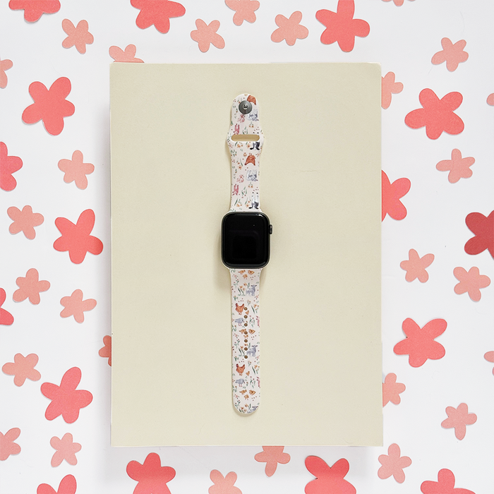 White Apple Watch strap with colorful animal and floral print, accented by pink flower confetti.