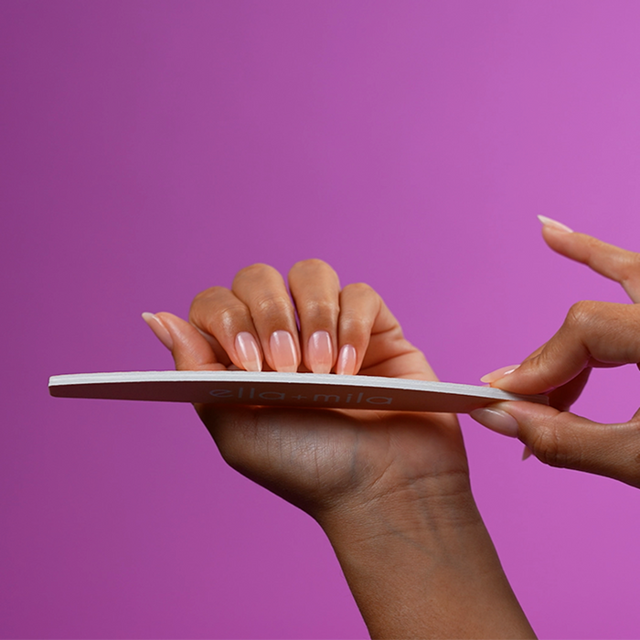 Filing nails with the peach half-moon nail file on a purple background