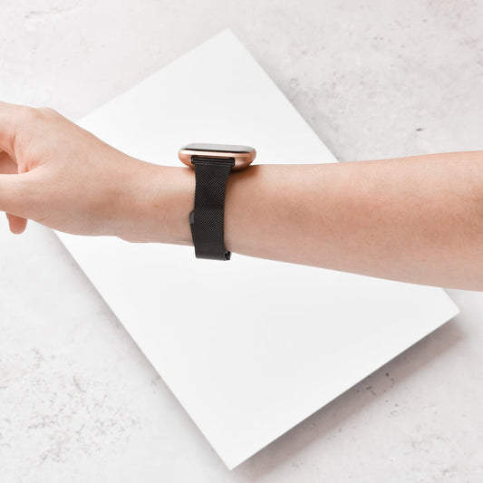 Black Slim Milanese Coconut Lane Fitbit strap worn on wrist, shown against a white and gray background.