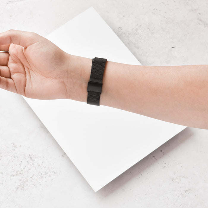 Black Slim Milanese Coconut Lane Fitbit strap on wrist, hand resting on white surface with blank sheet below.