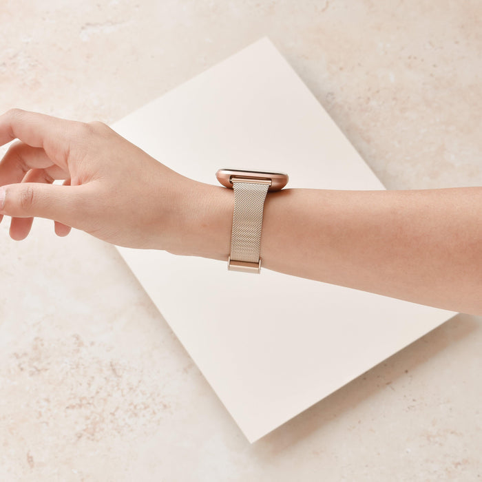 Gold Slim Milanese Coconut Lane Fitbit strap on a wrist, beige background, white card beneath the hand.