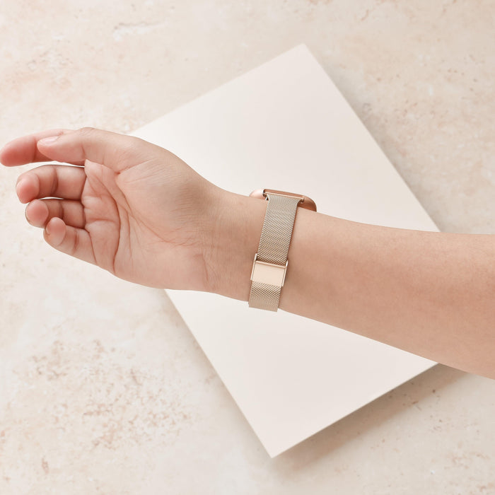 Gold Slim Milanese Coconut Lane Fitbit strap on a hand, shown against a light beige textured background.