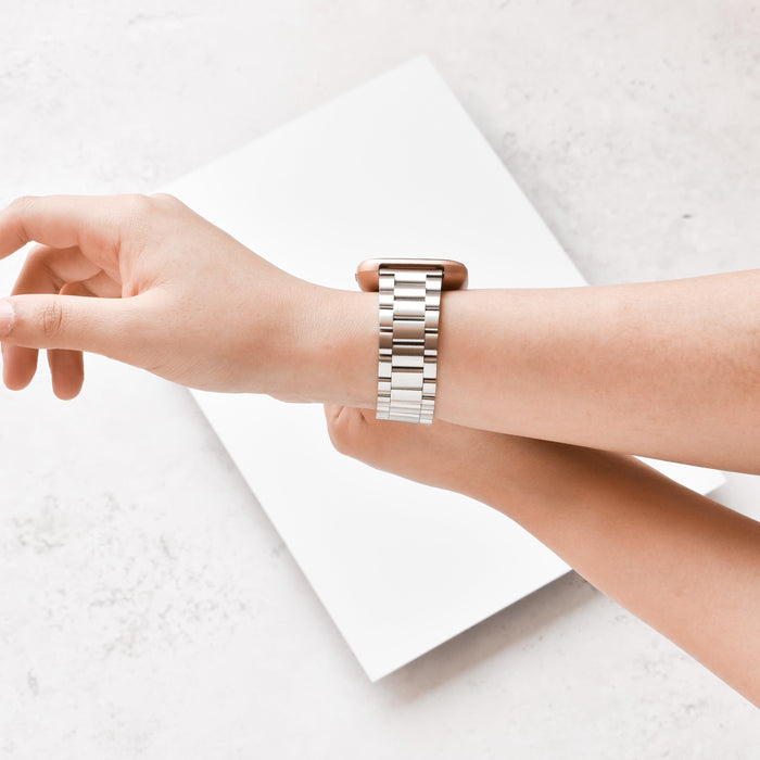 Hand adjusting a silver stainless steel Coconut Lane Fitbit strap on a white rectangular surface.