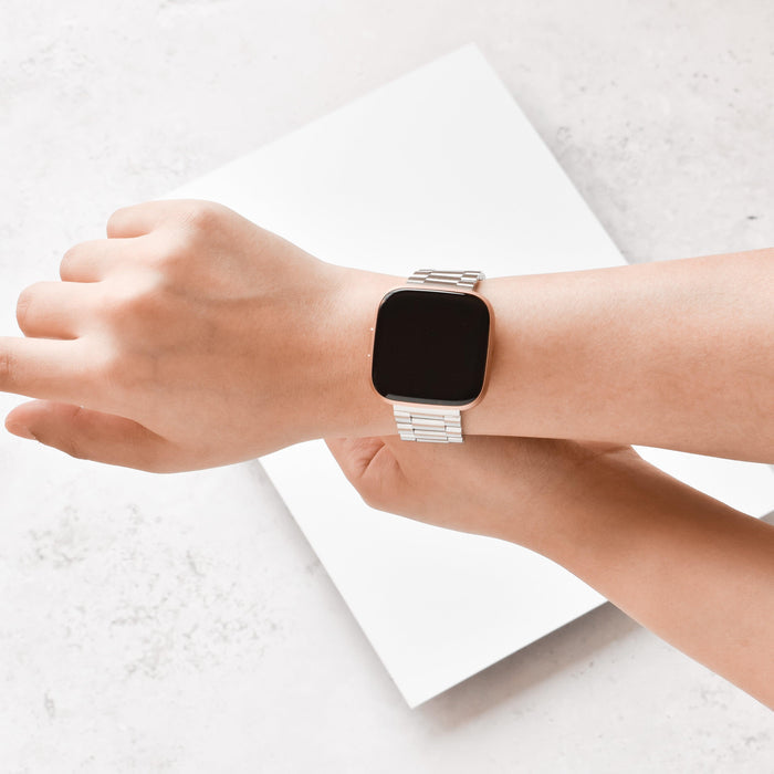 Silver Coconut Lane stainless steel Fitbit strap on a wrist, set against a plain light background.