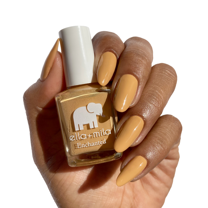 Goldie neutral golden mustard nail polish on a deep skin tone, holding the bottle