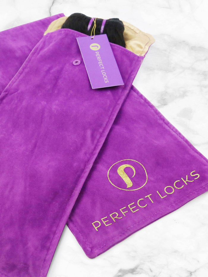The Perfect Locks Hair Extension Storage Pouch in purple suede with gold branding and tag, resting on a light marble surface.